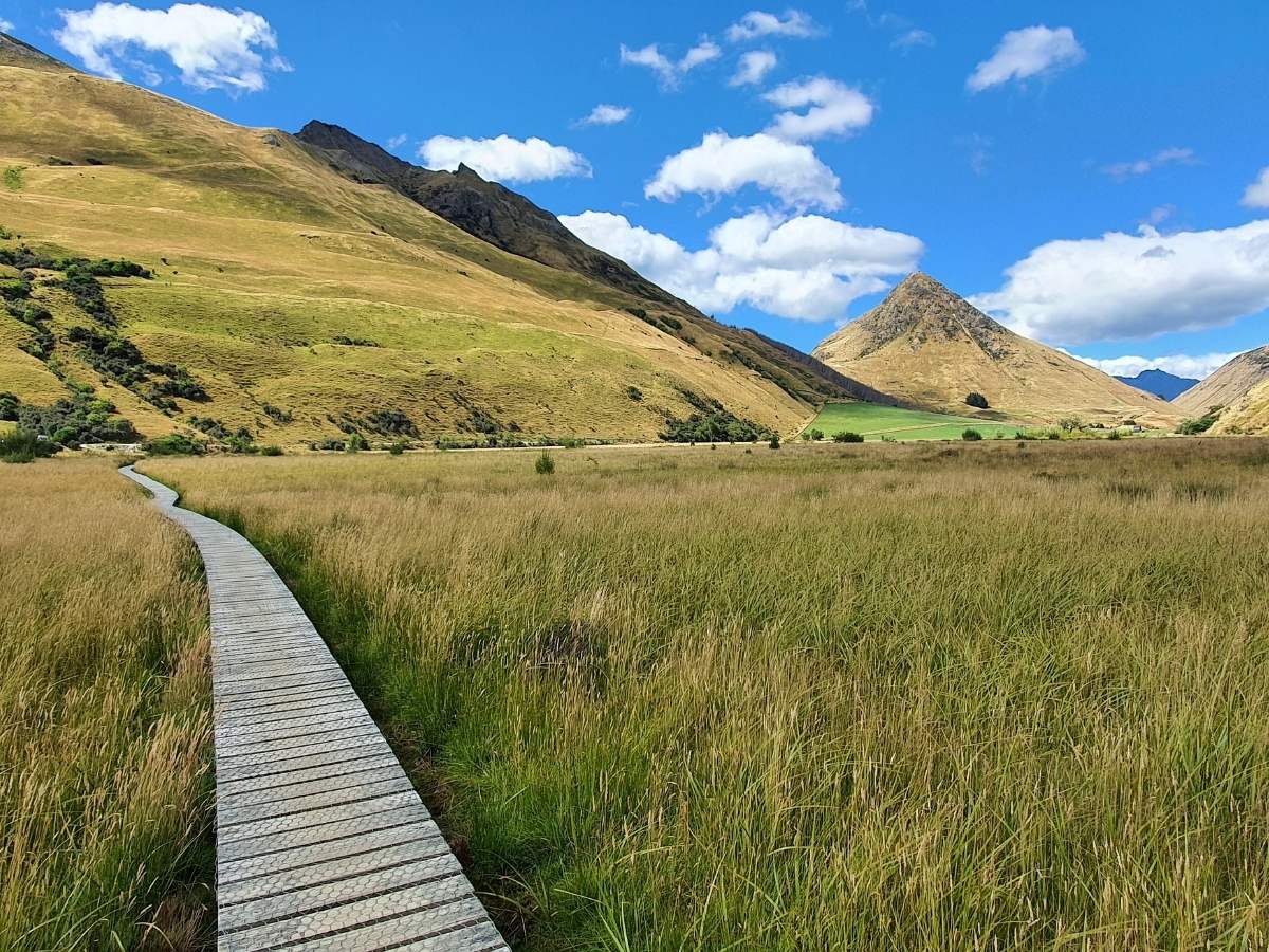 Wooden boardwalk through wetland grassland on the Moke Lake loop track with mountains behind, Queenstown
