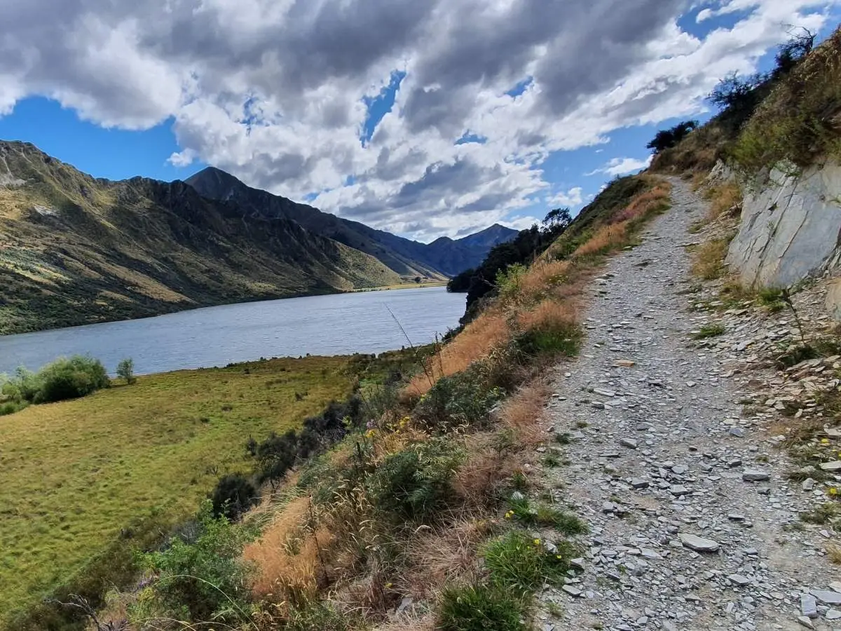 Gravel track alongside Moke Lake with mountains and cloudy sky, Queenstown