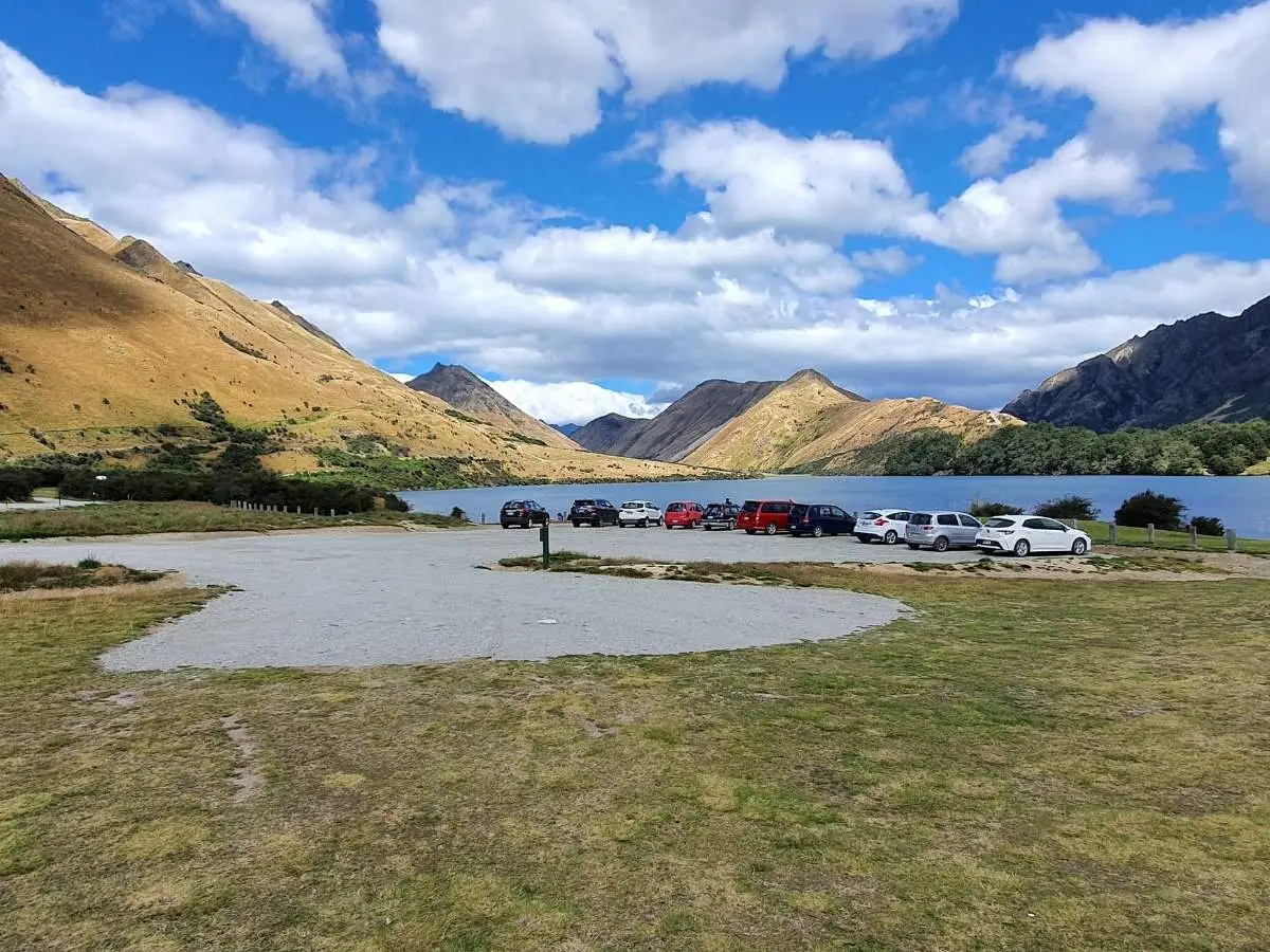 Large gravel car park at Moke Lake Reserve with lake and mountains behind, Queenstown