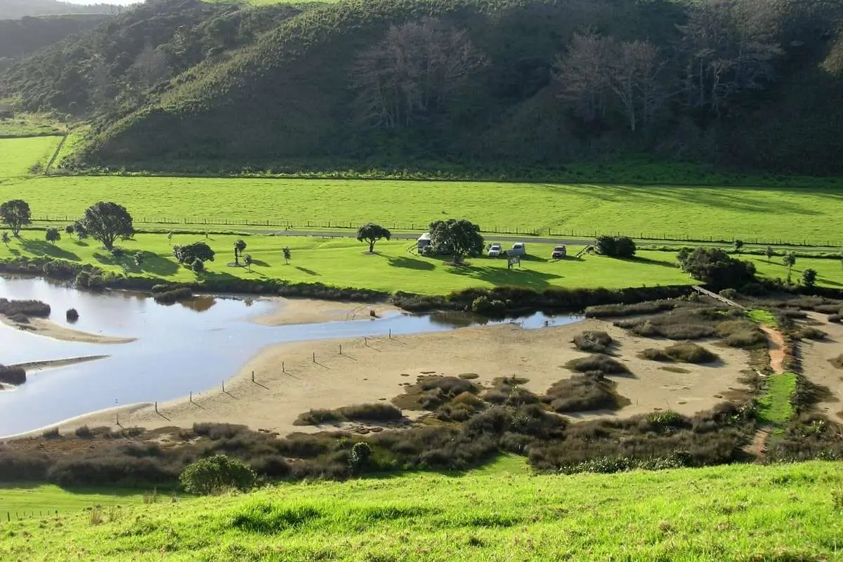 Aerial view of Tāwharanui lagoon outlet, campground and green farmland