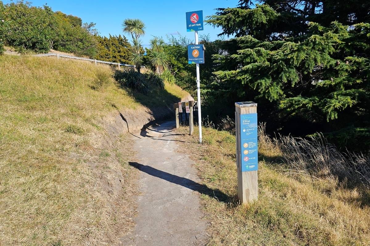 a path leading uphill through a field with a signpost in the distance