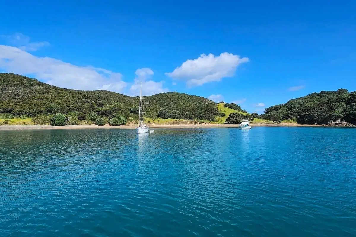 Turquoise water of Army Bay with anchored yacht and forested Moturua Island shoreline