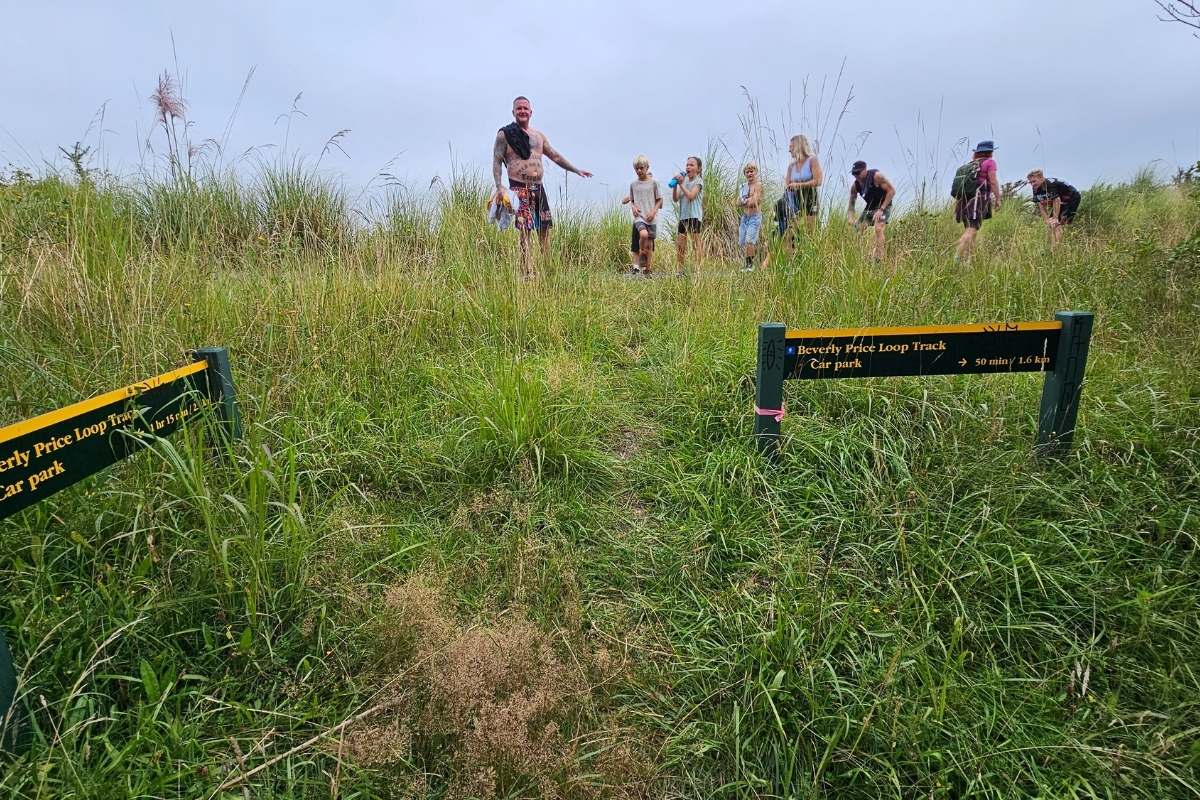 Group of adults and kids from ECC by Evana walking through long grass on track at top of Beverley Price Loop with countryside views
