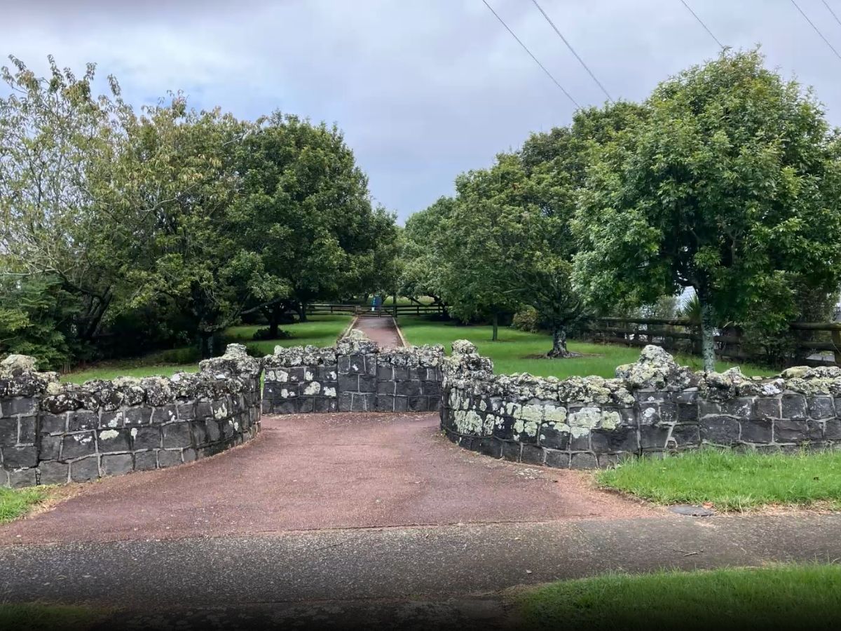Volcanic stone wall with pathway entrance leading into Cornwall Park with mature trees and green grass beyond