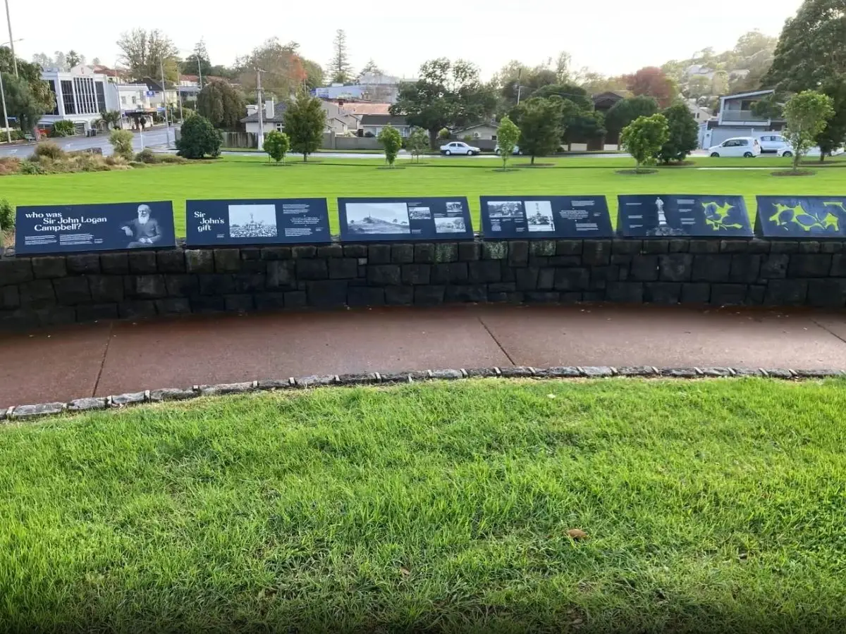 Row of dark blue information panels mounted on stone wall showing historical photos and text about Sir John Logan Campbell and Cornwall Park