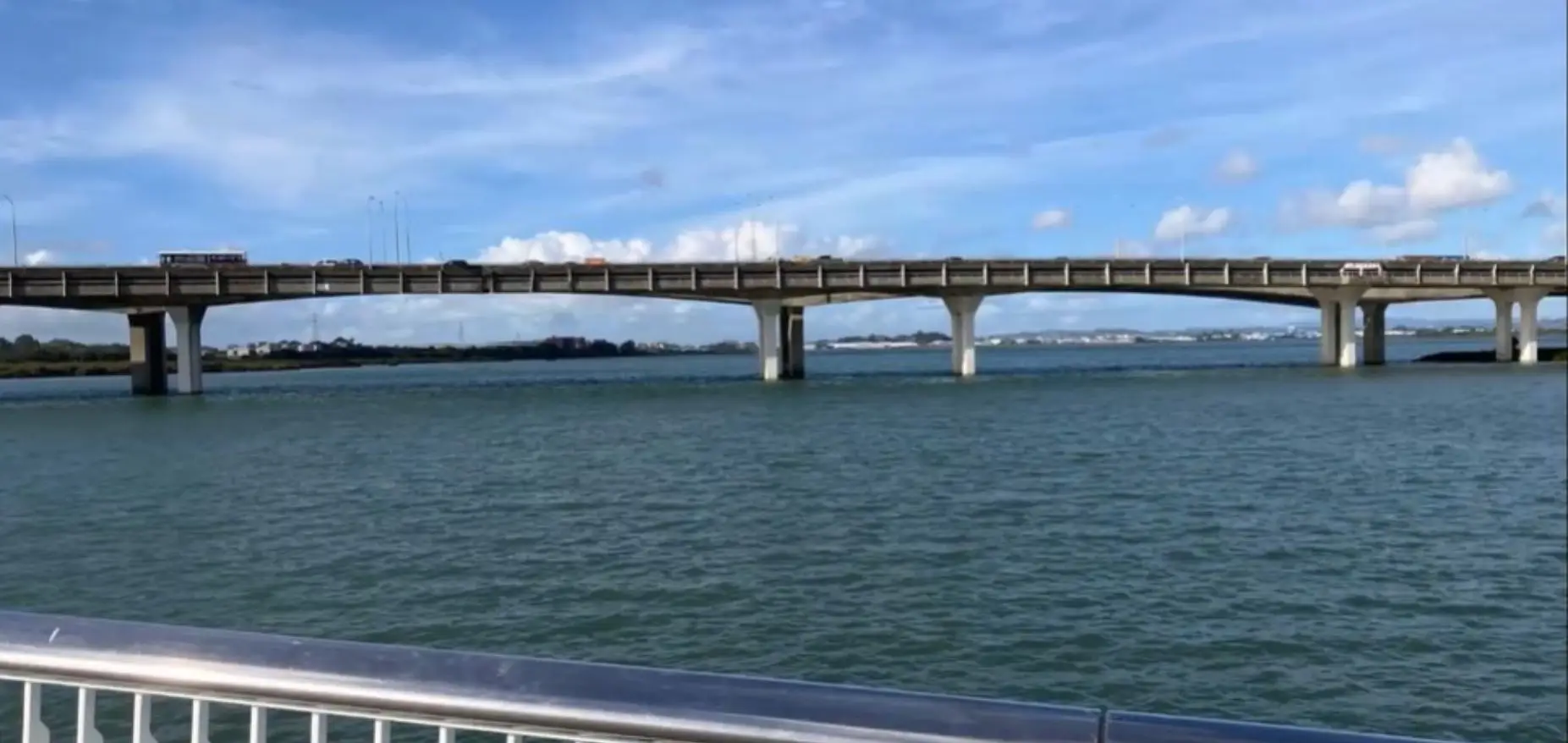 View of Mangere Bridge motorway crossing over Manukau Harbour from the new walking and cycling bridge, with white railings in foreground