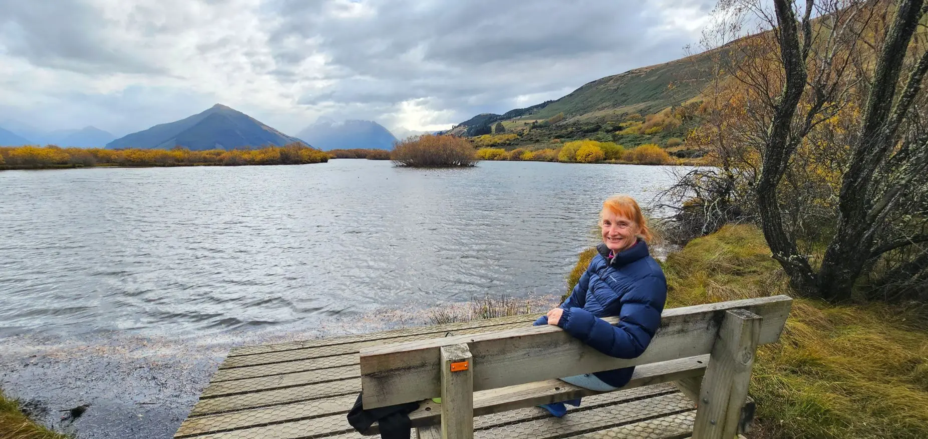 Walker resting on a bench at Glenorchy Southern Lagoon with mountain views and autumn colour, May 2026