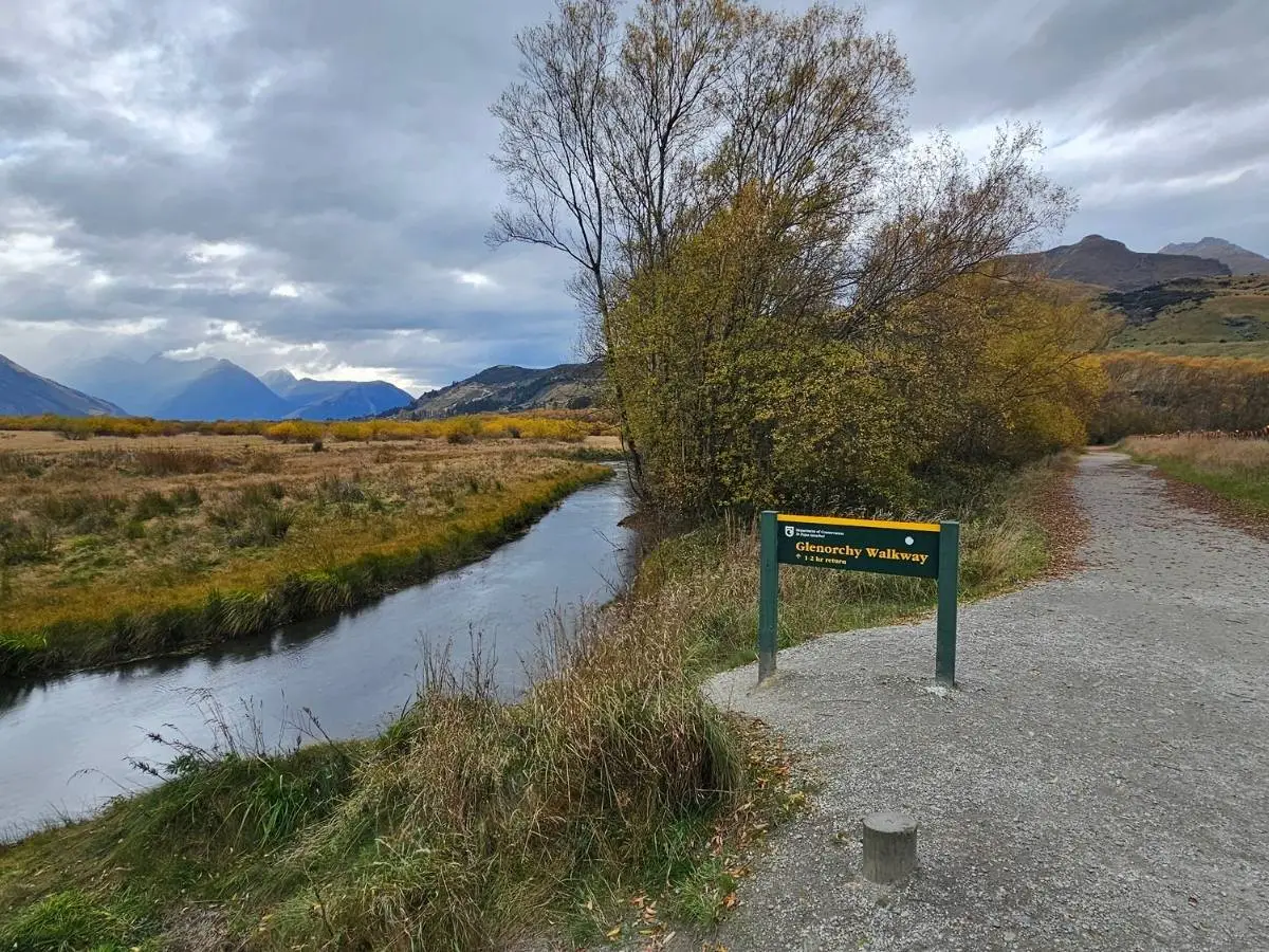 DOC sign at the start of the Glenorchy Walkway with wide gravel track, wetlands and mountains beyond