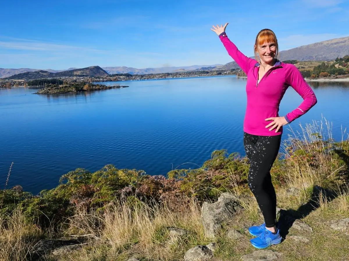 Sandra at a viewpoint above Lake Wanaka with Ruby Island and Wanaka town in the background, May 2026